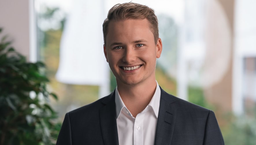 Portrait of Benedikt Krümmel in formal attire with a white shirt and dark jacket, taken in a modern office.
